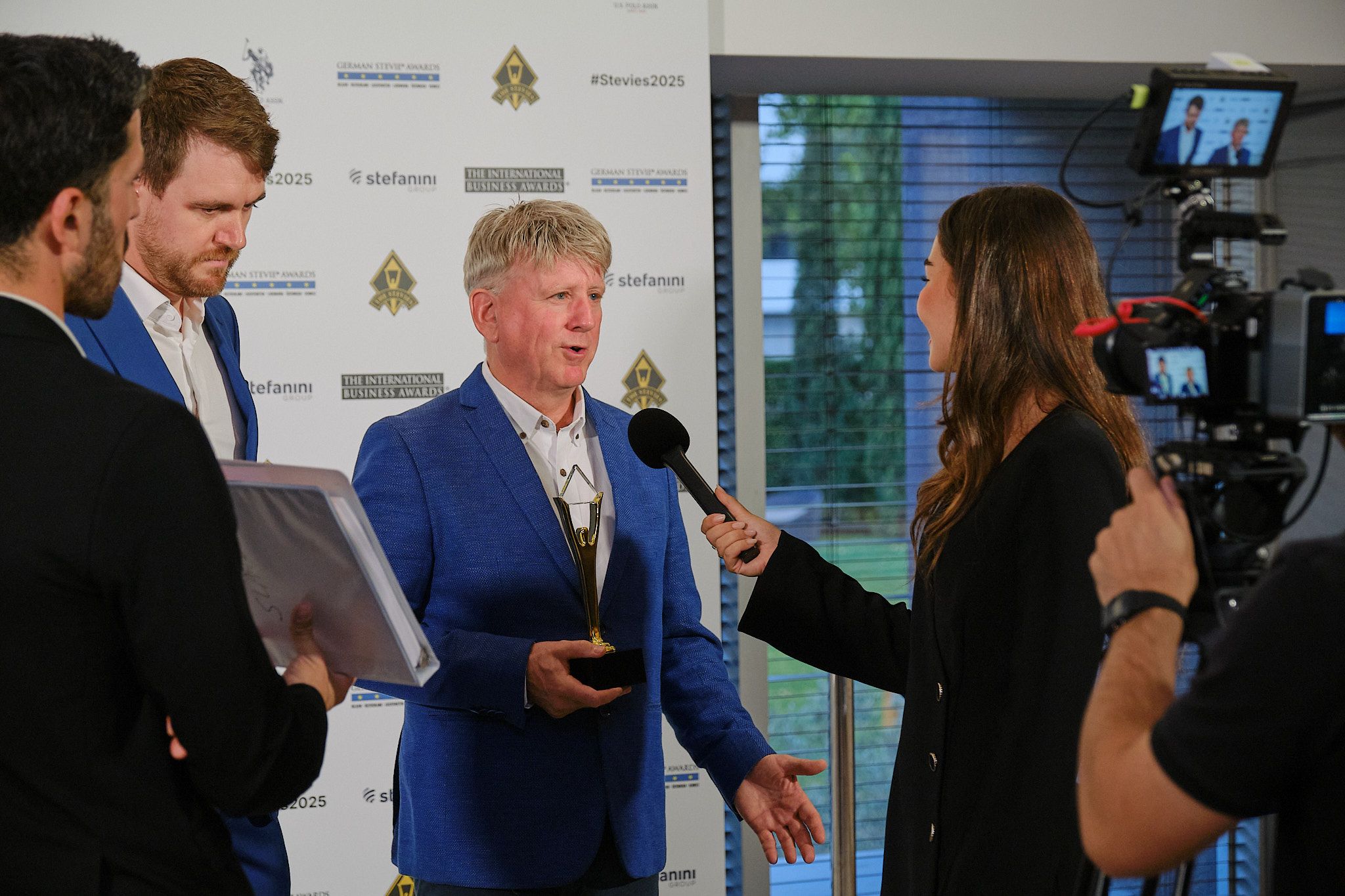 Ganador con chaqueta azul siendo entrevistado en la alfombra roja de los International Business Awards® 2025