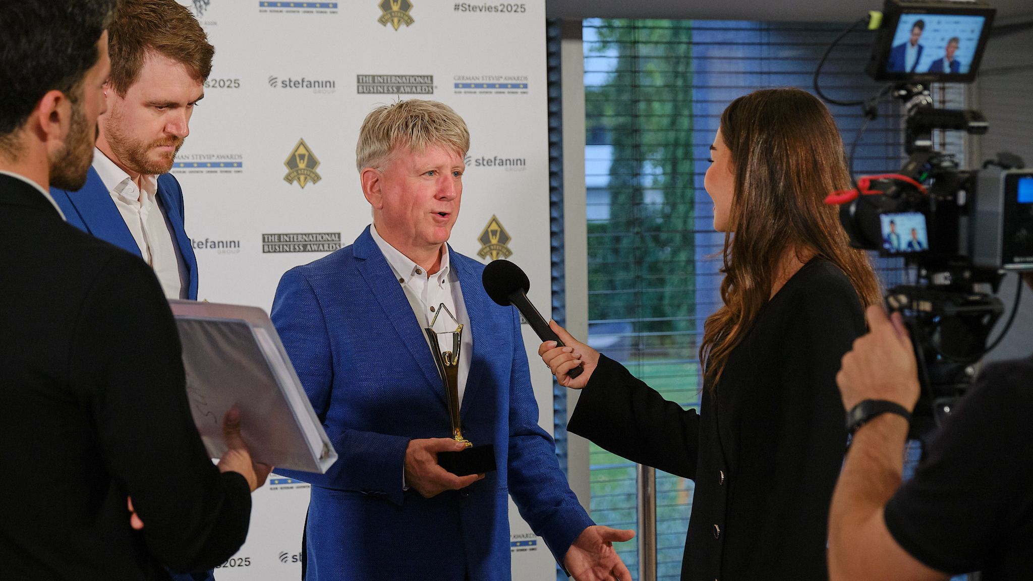 Ganador con chaqueta azul siendo entrevistado en la alfombra roja de los International Business Awards® 2025