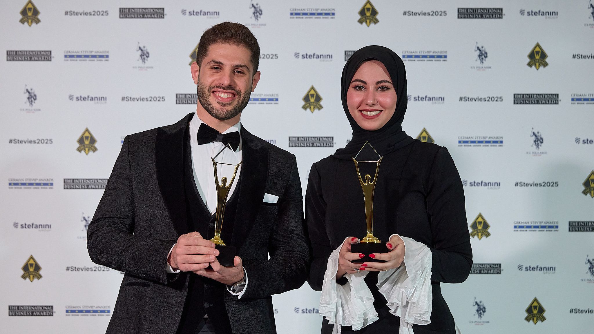 Dos ganadores de los International Business Awards® 2025 sosteniendo sus trofeos Stevie de oro en la alfombra roja