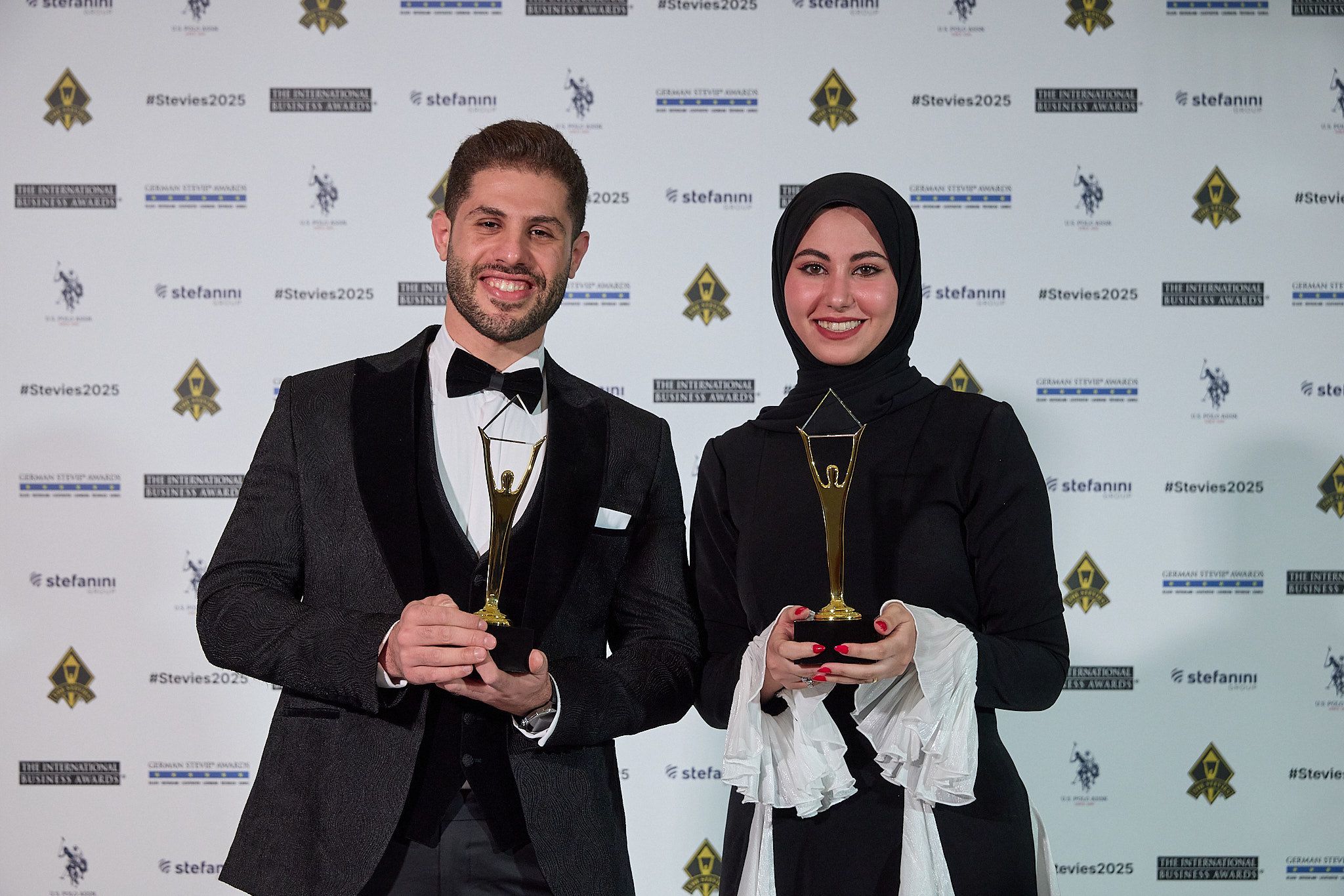 Dos ganadores de los International Business Awards® 2025 sosteniendo sus trofeos Stevie de oro en la alfombra roja