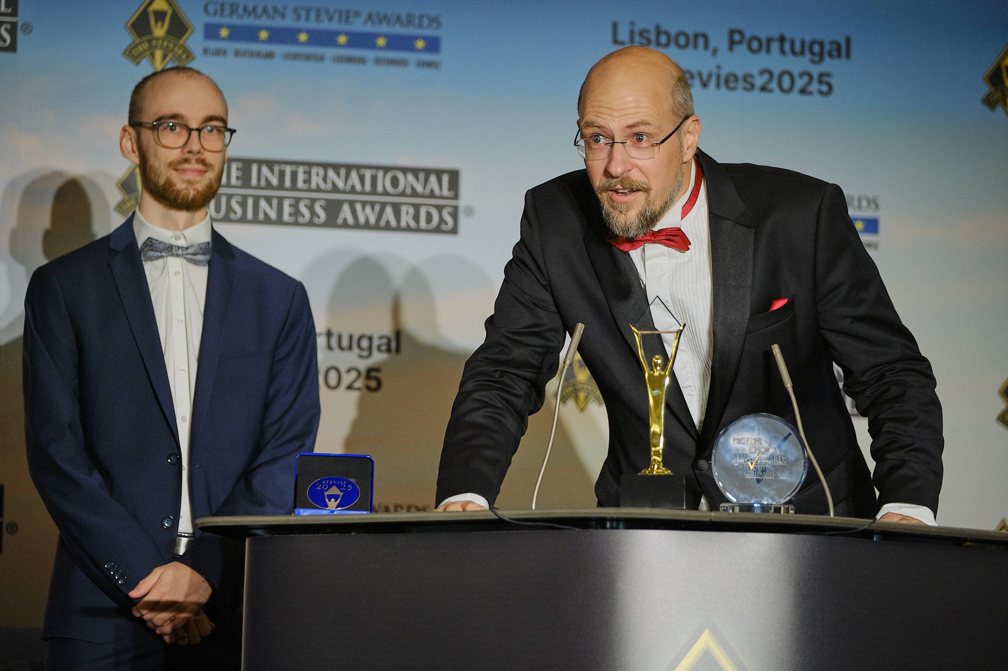 Ganador pronunciando su discurso de agradecimiento junto a otro galardonado en los International Business Awards® 2025